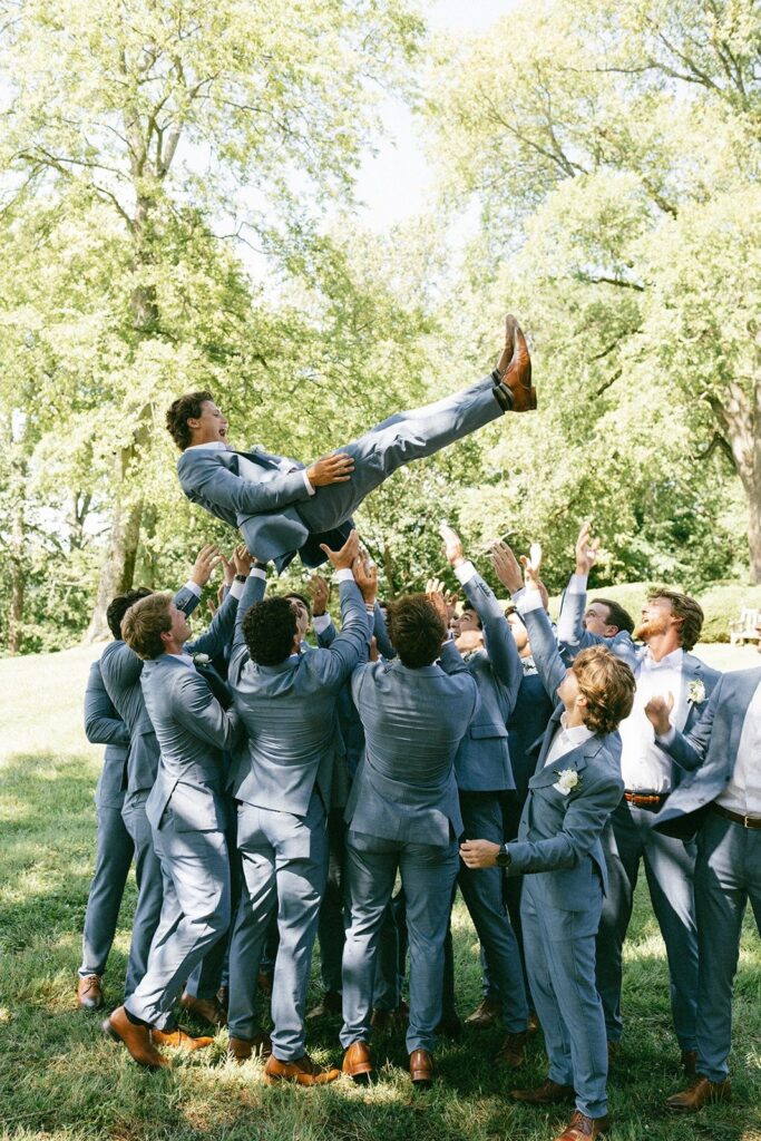 groom tossed in the air by groomsmen in matching blue suits during an outdoor wedding celebration in Nashville, Tennessee