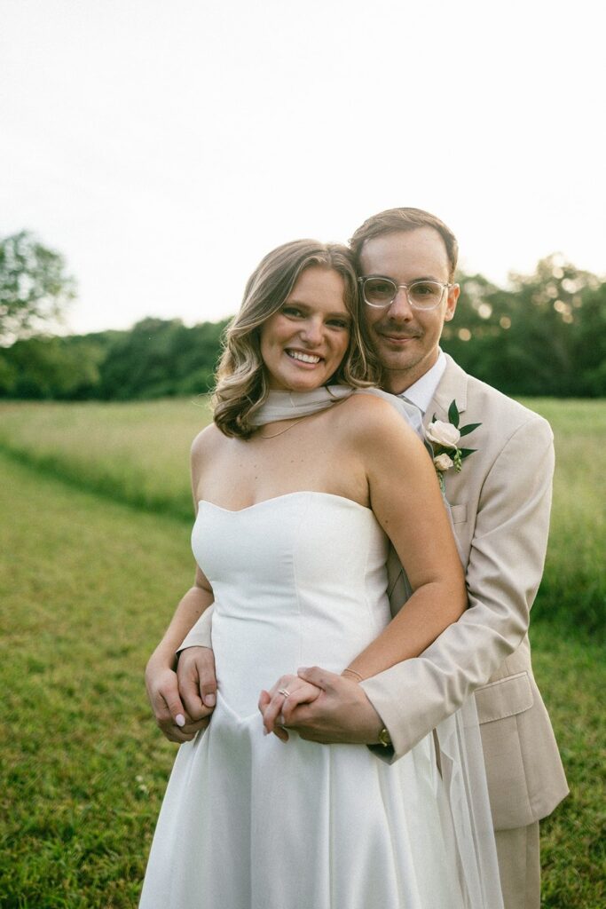bride and groom embracing in a green field at sunset, captured by one of the top Nashville wedding photographers