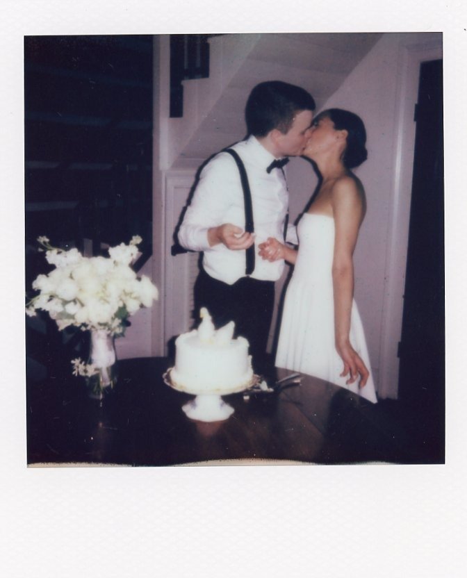 newlyweds sharing a kiss beside their wedding cake in a nostalgic instant photo by a Nashville TN wedding photographer