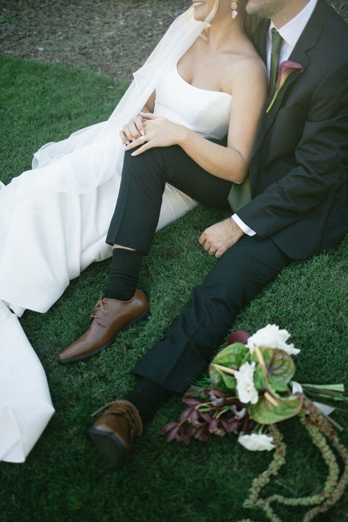 bride and groom sitting on lush green grass with bouquet beside them in an intimate portrait by one of the top Nashville wedding photographers