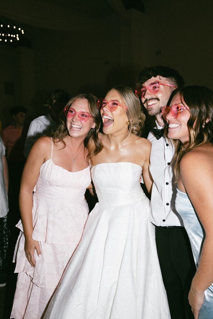 bride and friends wearing pink heart sunglasses laughing on the dance floor at a nashville tn wedding reception