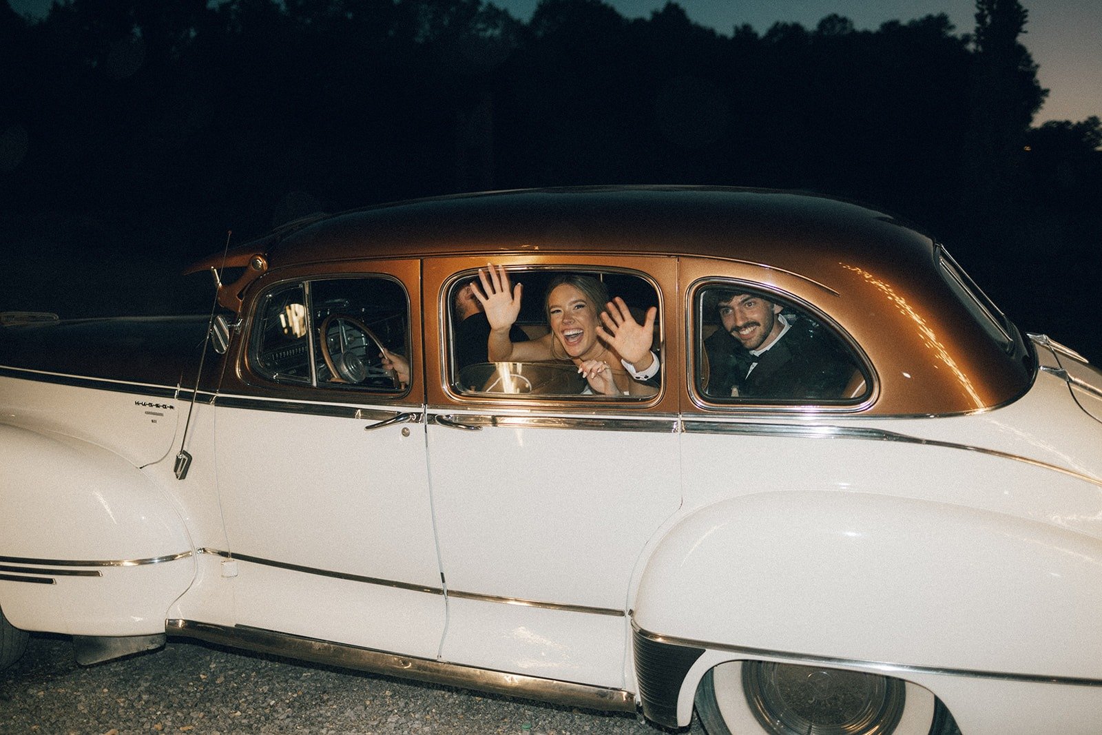 newlyweds waving from a vintage getaway car at night, captured by the top Nashville wedding photographers