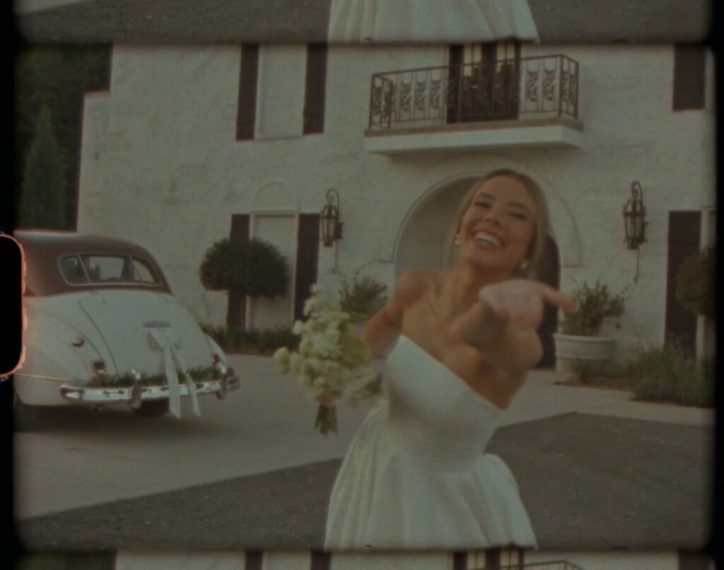bride smiling and reaching toward the camera in front of a vintage getaway car at a Nashville Tennessee wedding
