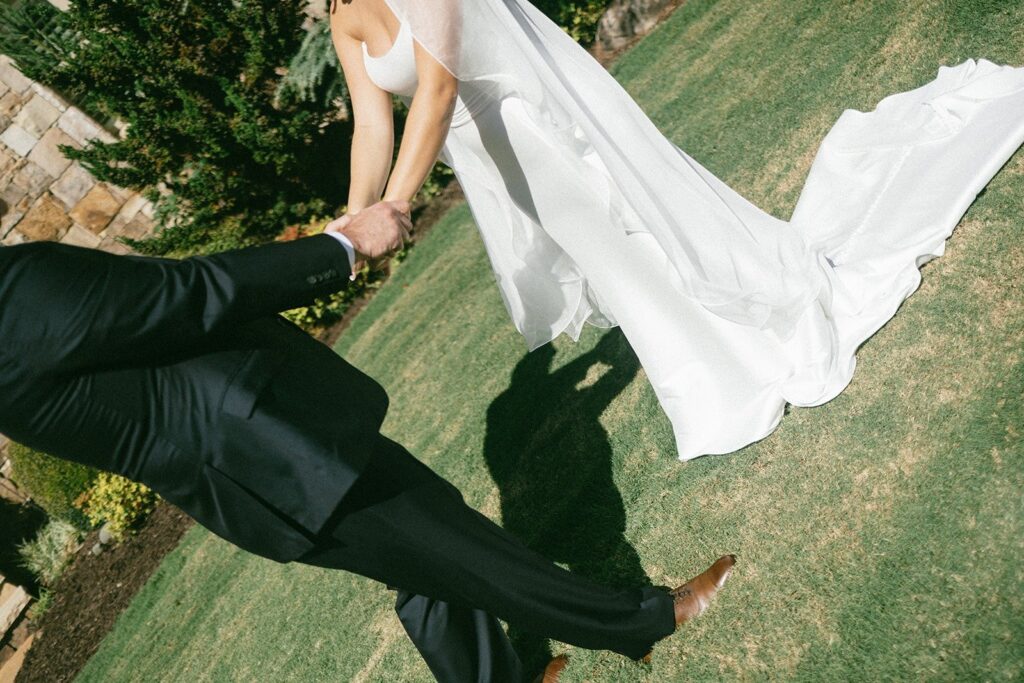 bride and groom holding hands and running across a lawn in a candid moment captured by Nashville wedding photographers