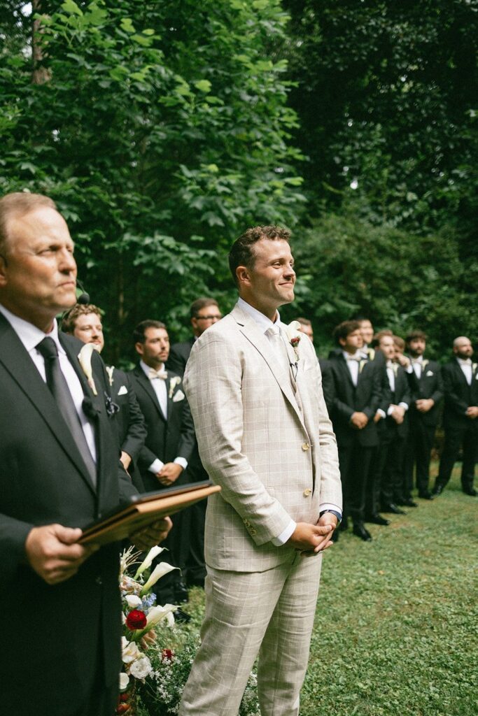 groom smiling during an outdoor ceremony with groomsmen in black tuxedos, photographed by a Nashville TN wedding photographer