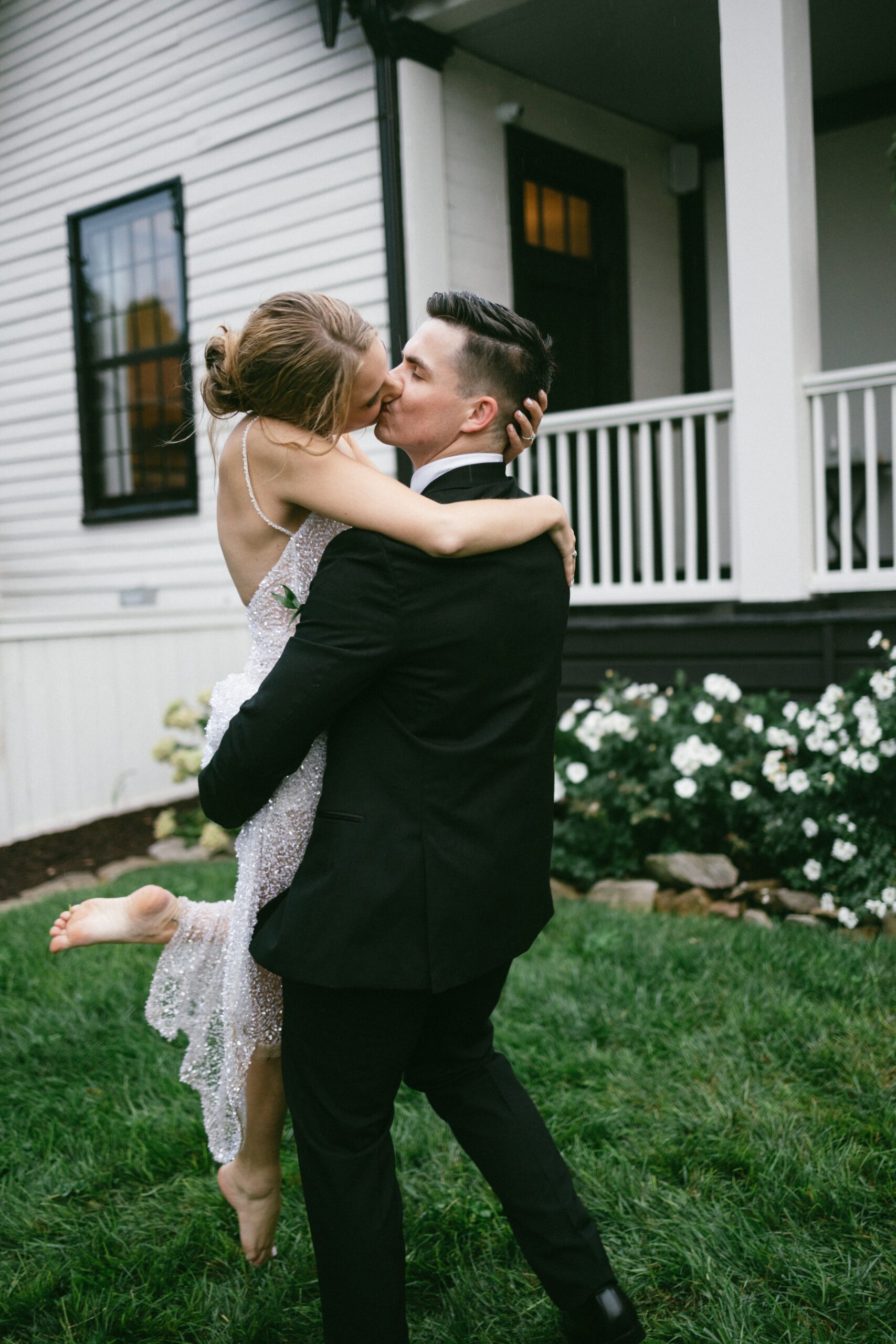 Newlyweds sharing a playful kiss as the groom lifts the bride outside a classic white venue, showcasing the charm of small wedding chapels in Nashville TN.