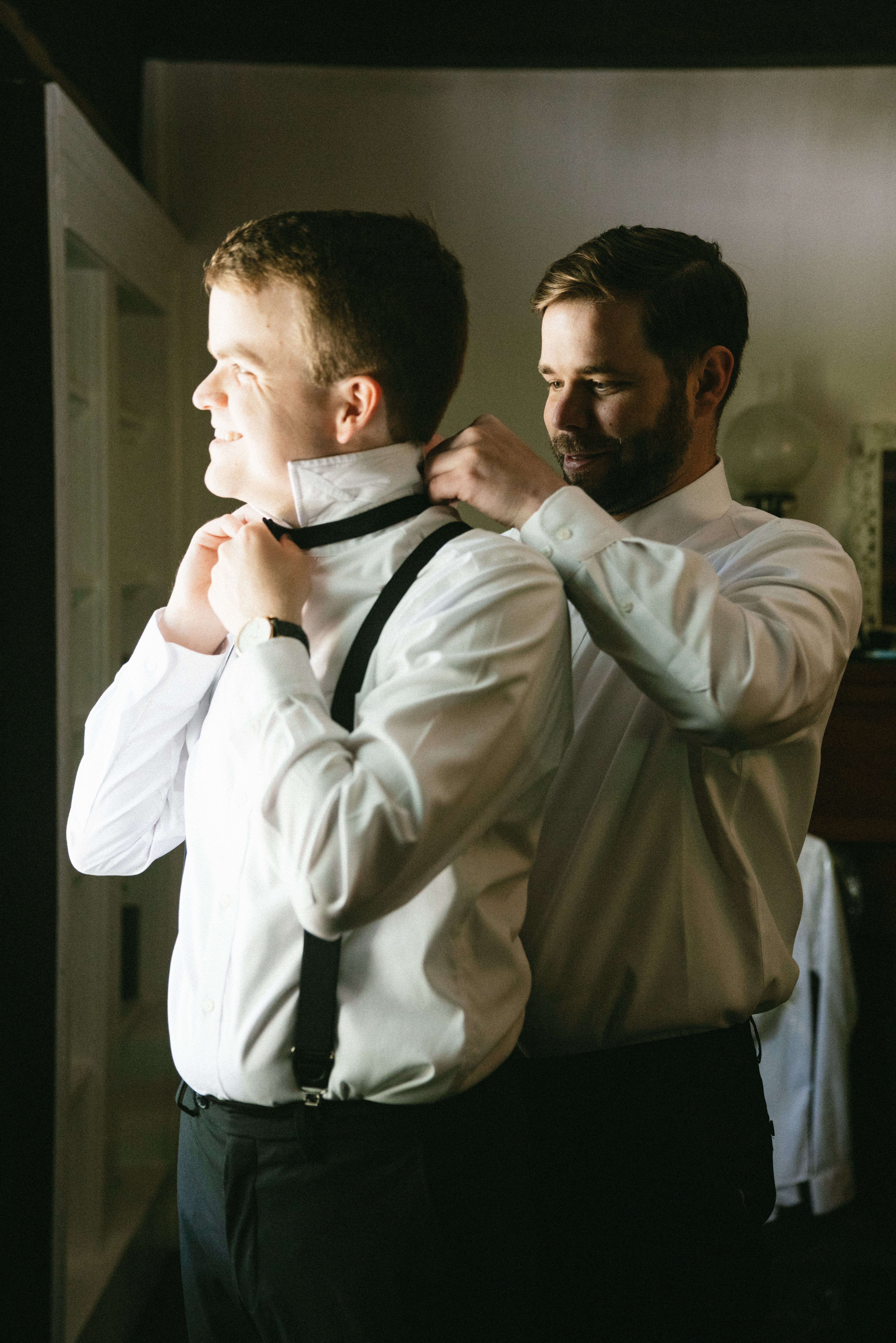 Best man helping the groom adjust his bow tie and suspenders during wedding preparations at one of the charming small wedding venues near Nashville TN.