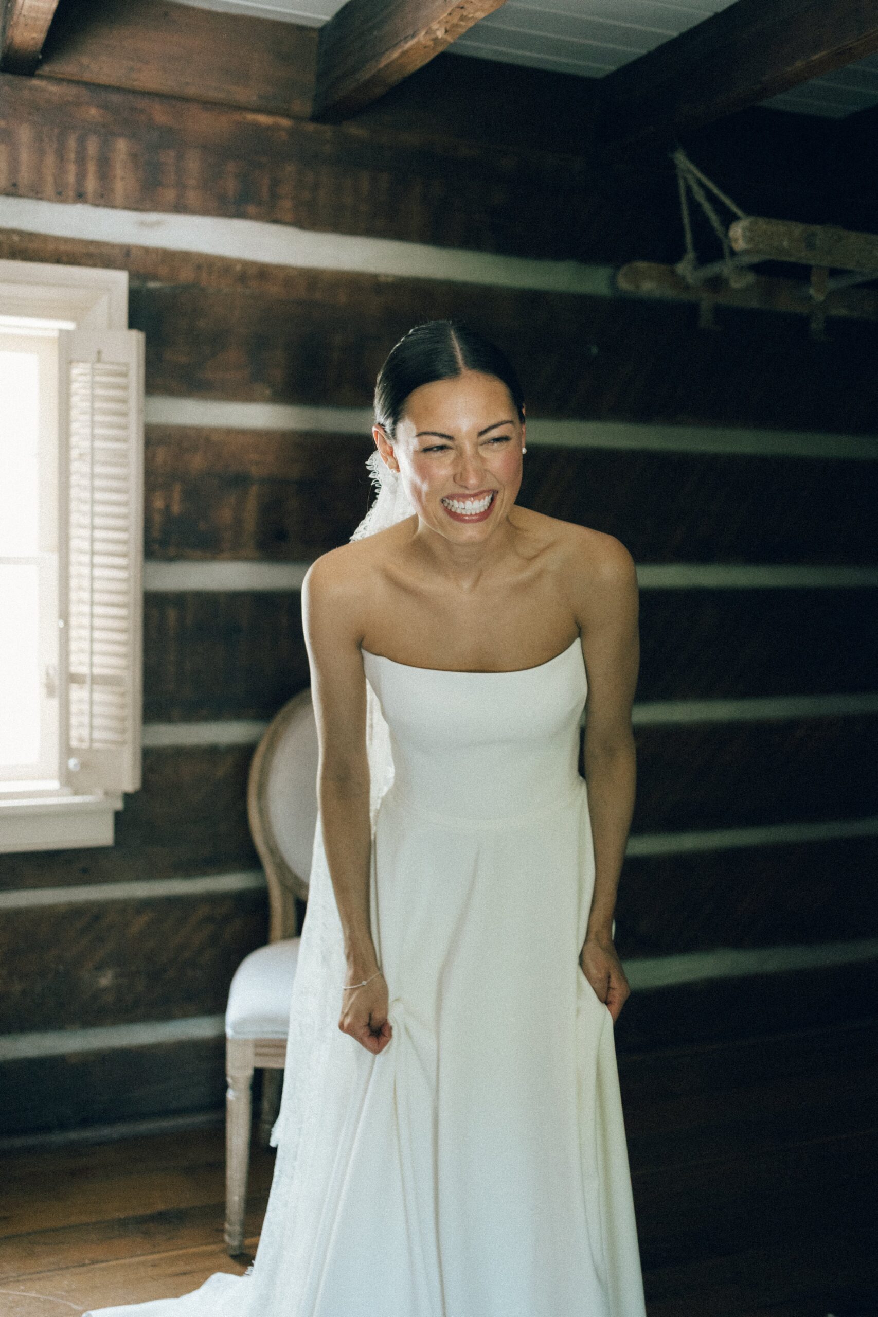 Bride laughing in her minimalist wedding dress while getting ready in a cozy log cabin room at one of the charming small wedding chapels in Nashville TN.