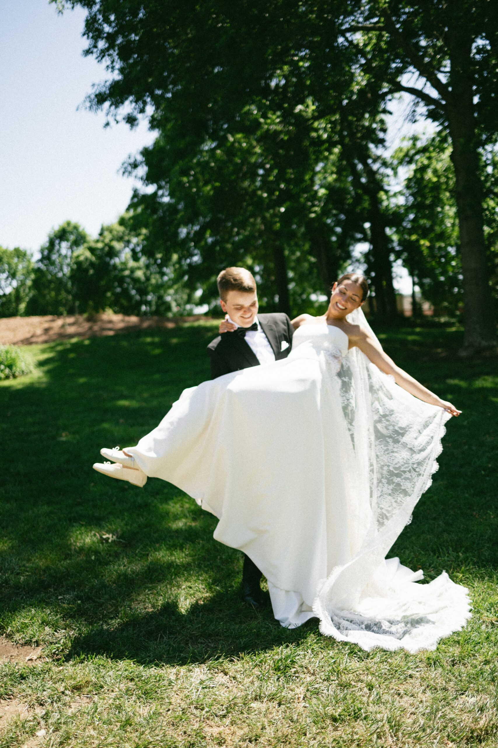 Groom lifting the bride in her flowing wedding dress and veil during joyful outdoor portraits at one of the charming small wedding venues near Nashville TN.