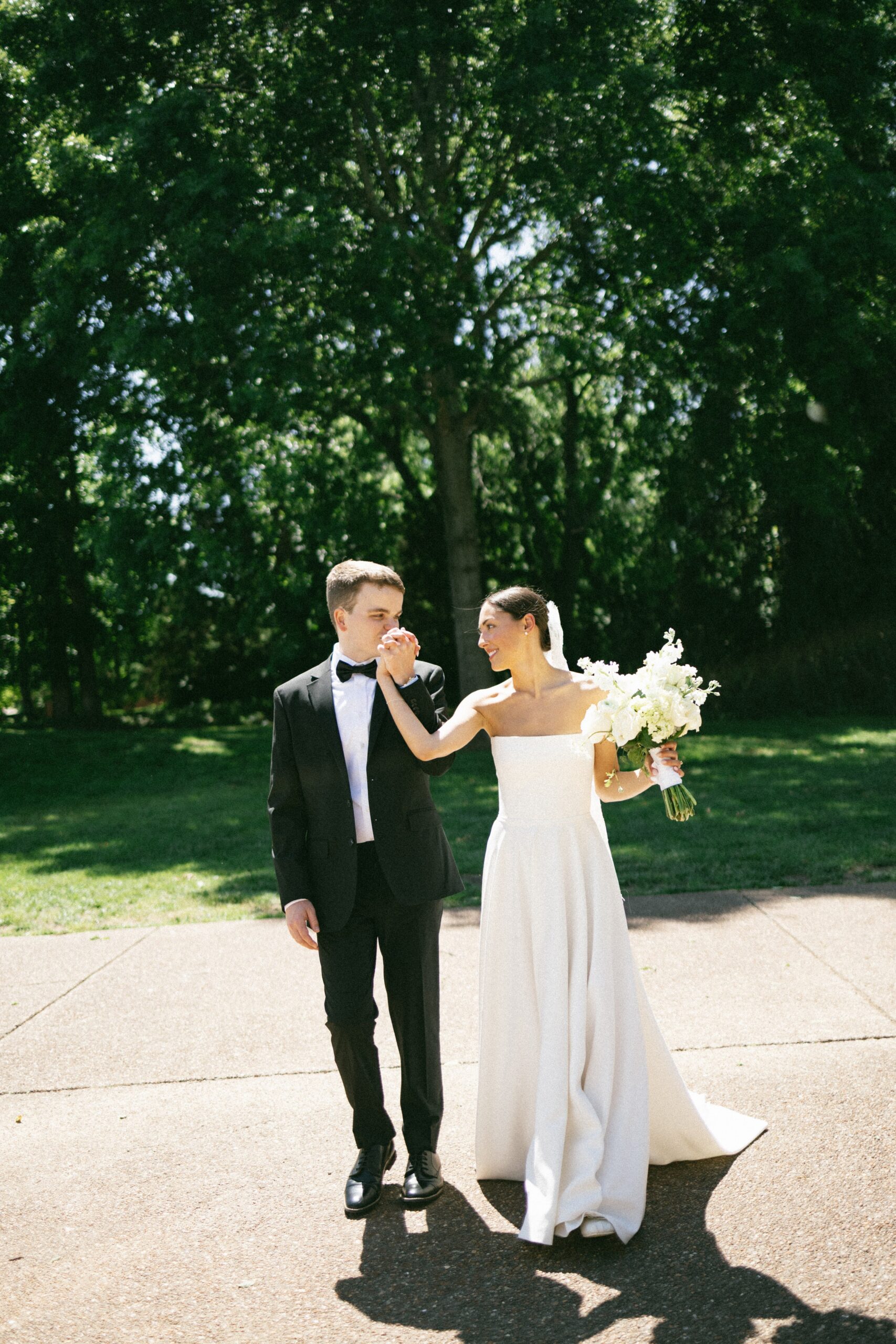 Bride holding a bouquet and leading the groom by the hand along a sunlit path after their ceremony at one of the most intimate wedding venues in Nashville TN.