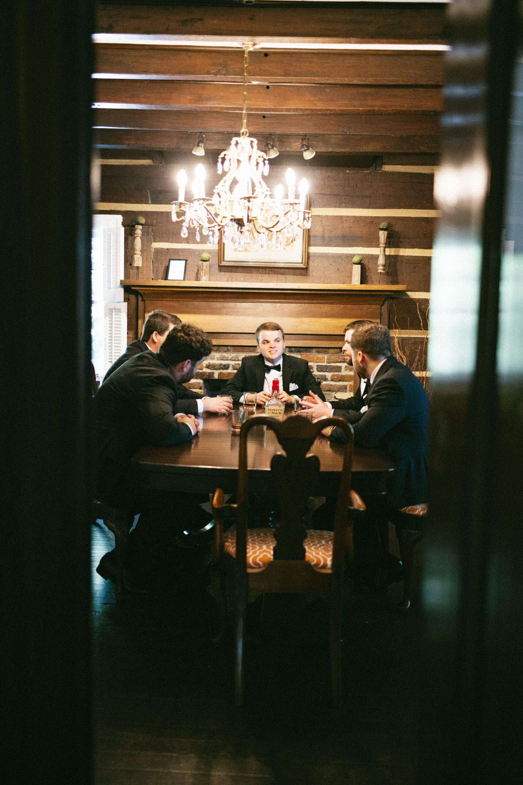 Groom and groomsmen sharing drinks and conversation around a wooden table beneath a chandelier at one of the intimate small wedding venues Nashville TN couples love.