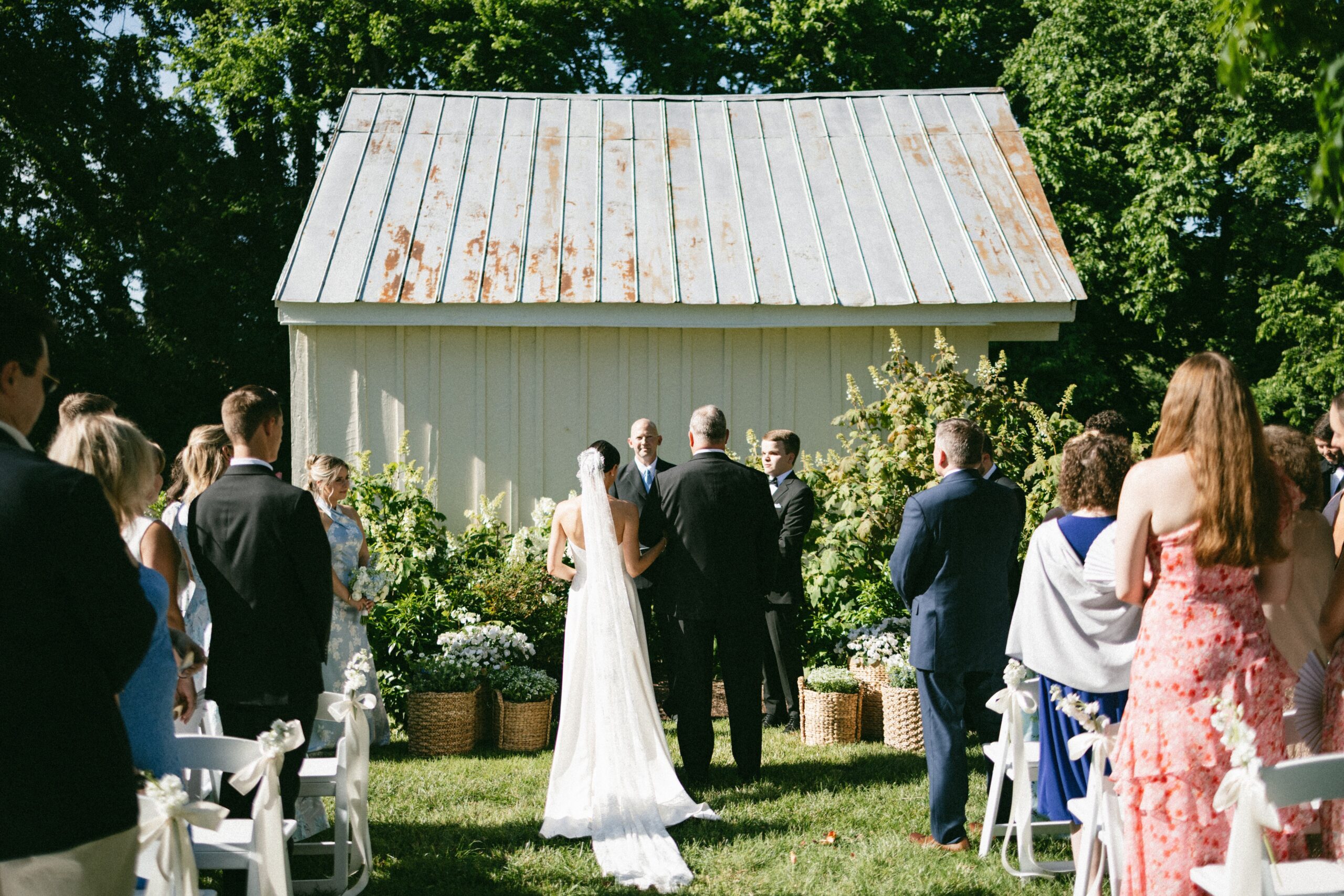 Bride walking down the aisle with her father during an outdoor garden ceremony beside a charming white chapel at one of the most romantic small wedding venues in Nashville TN.