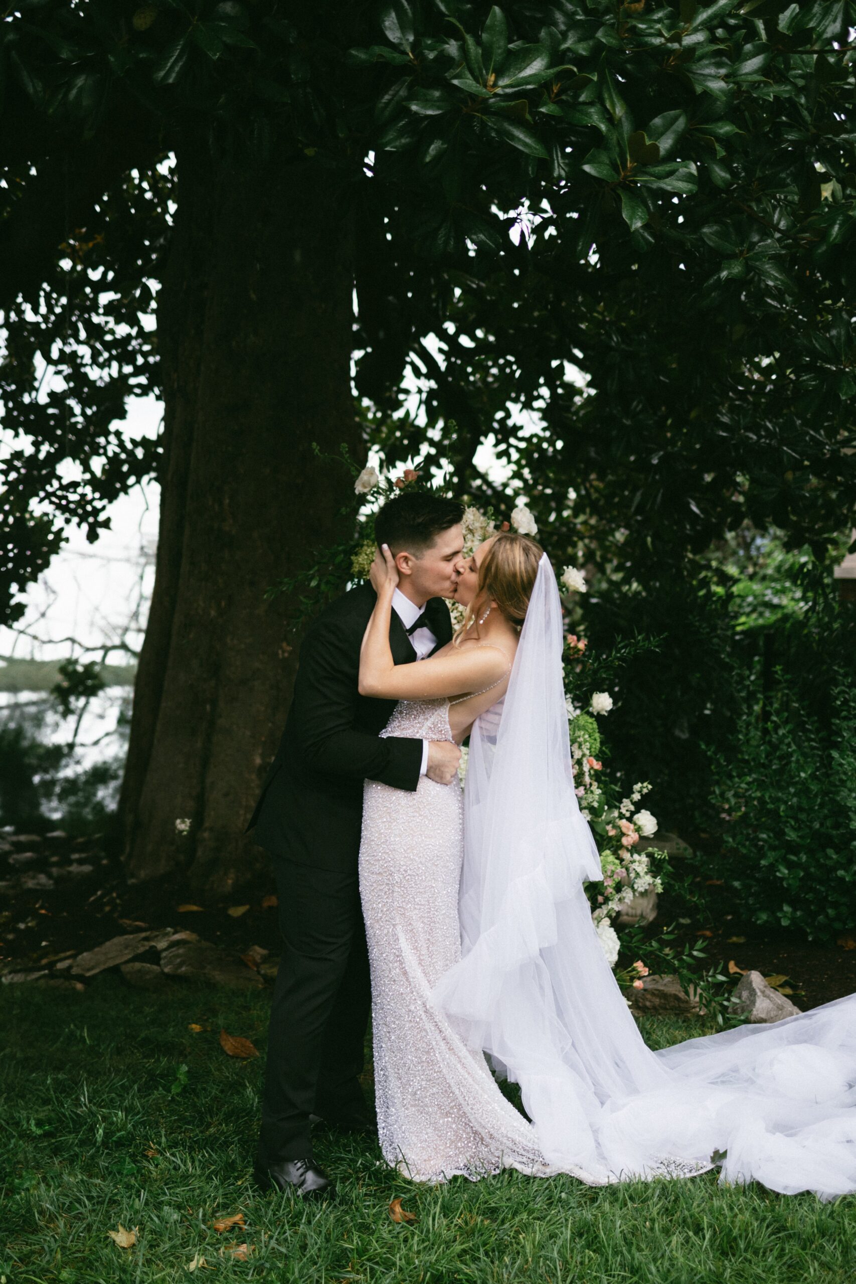 Bride and groom sharing a romantic kiss beneath towering magnolia trees during an outdoor ceremony at one of the most beautiful small wedding venues in Nashville TN.