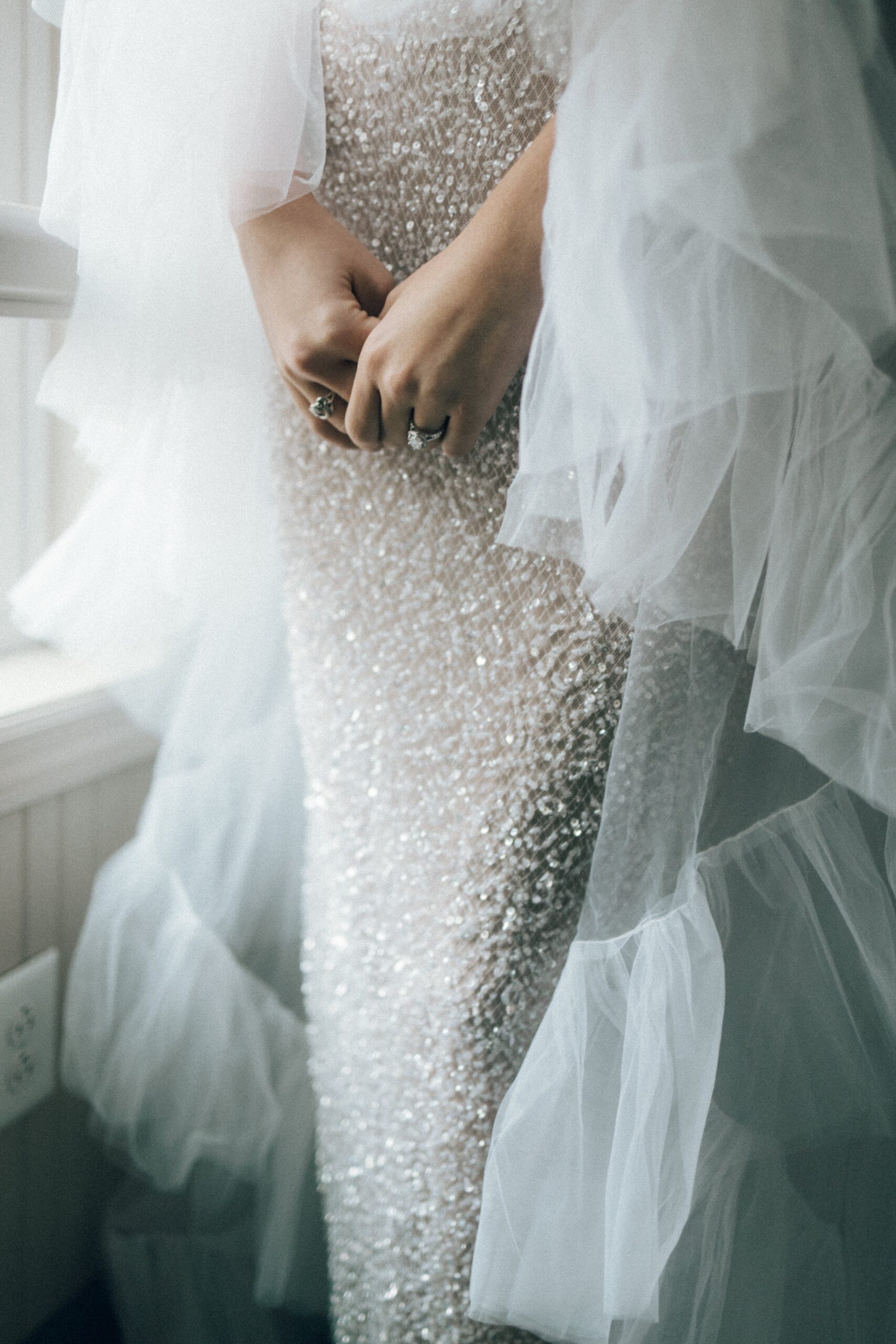 Bride adjusting her sparkling beaded wedding dress and veil beside a window while getting ready at one of the beautiful small wedding venues in Nashville TN.
