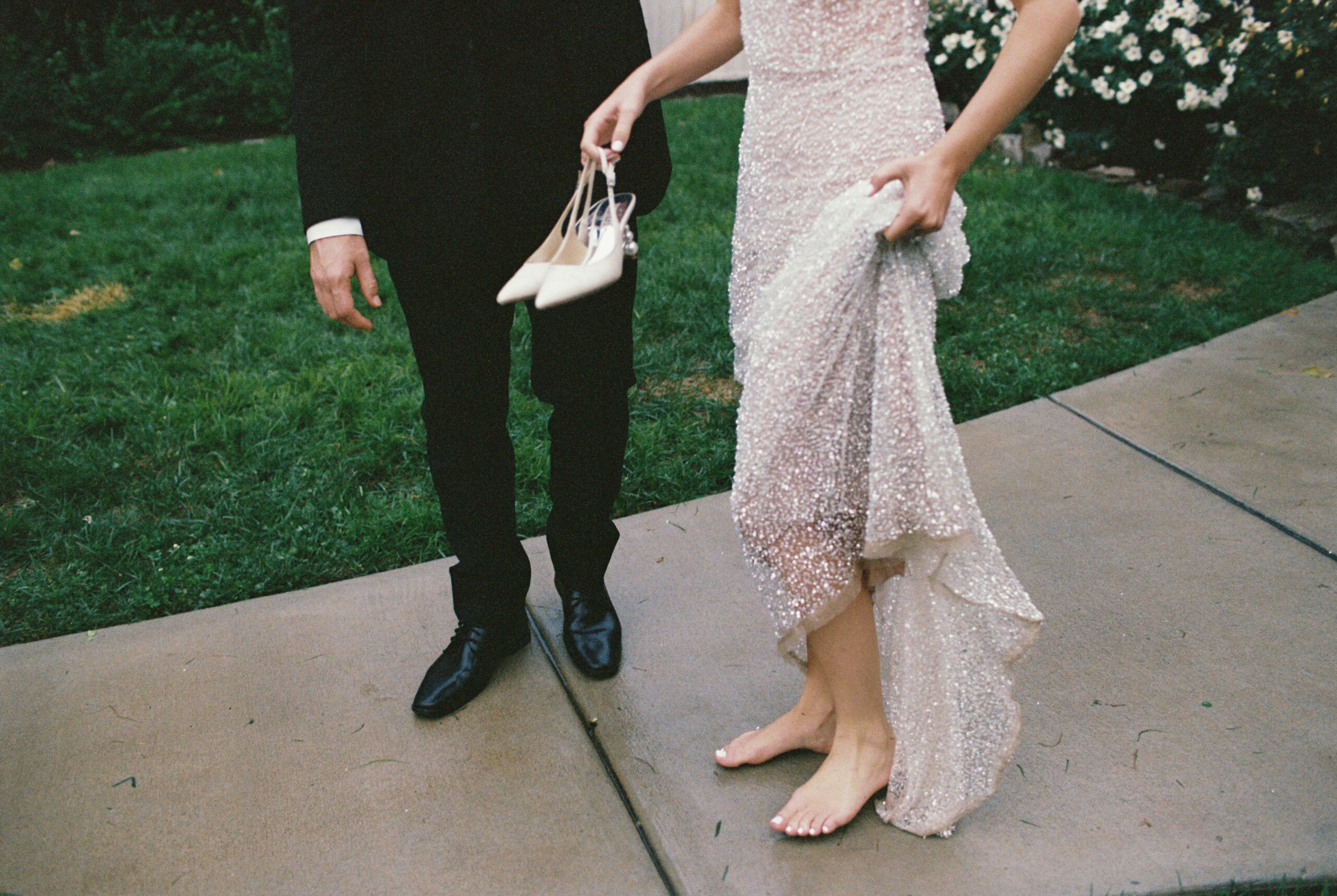 Bride walking barefoot while holding her heels and lifting her beaded wedding dress beside the groom outside one of the charming small wedding venues near Nashville TN.