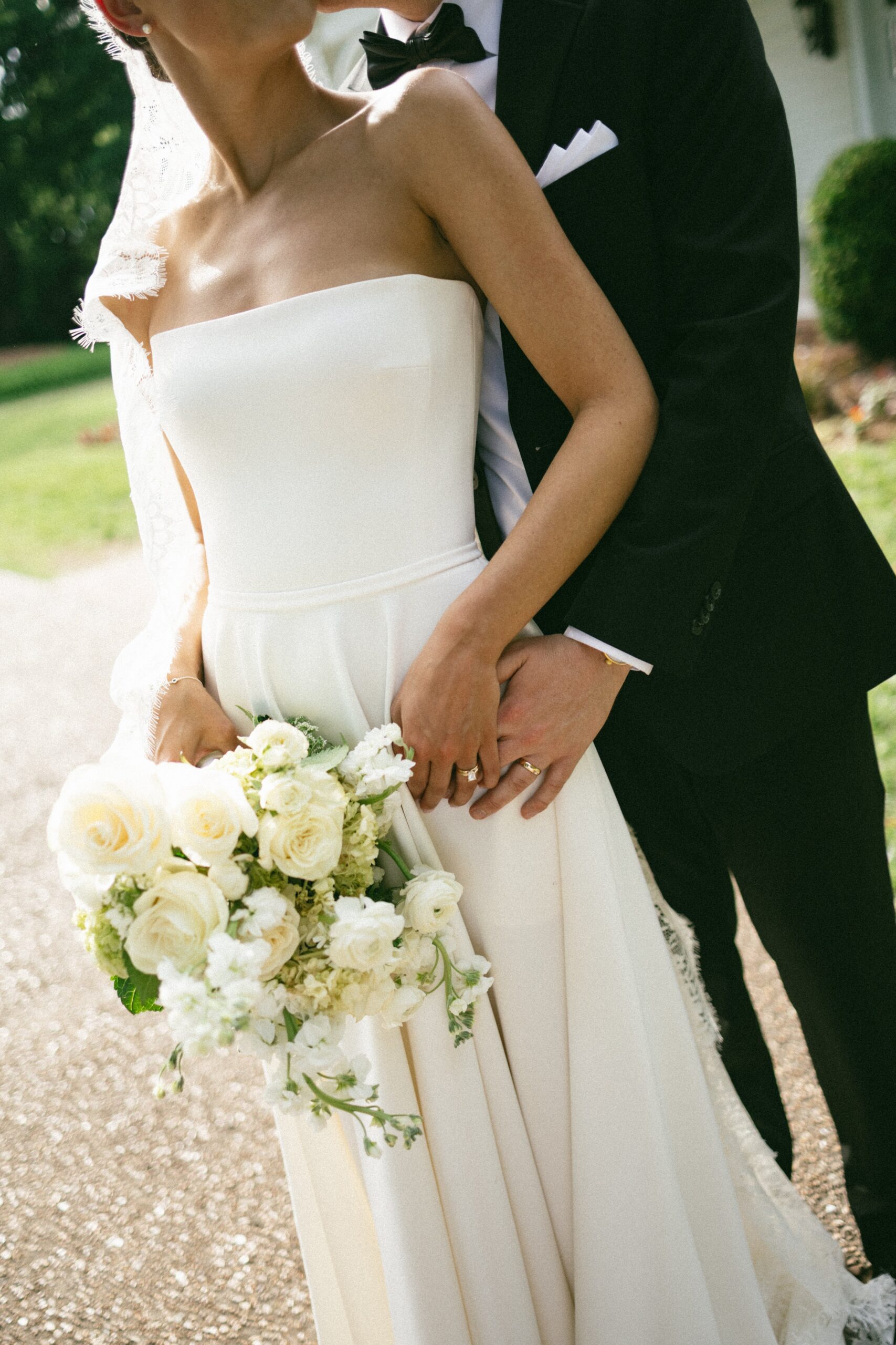 Groom standing behind the bride as she holds a bouquet of white roses during golden hour portraits at one of the beautiful small wedding venues in Nashville TN.