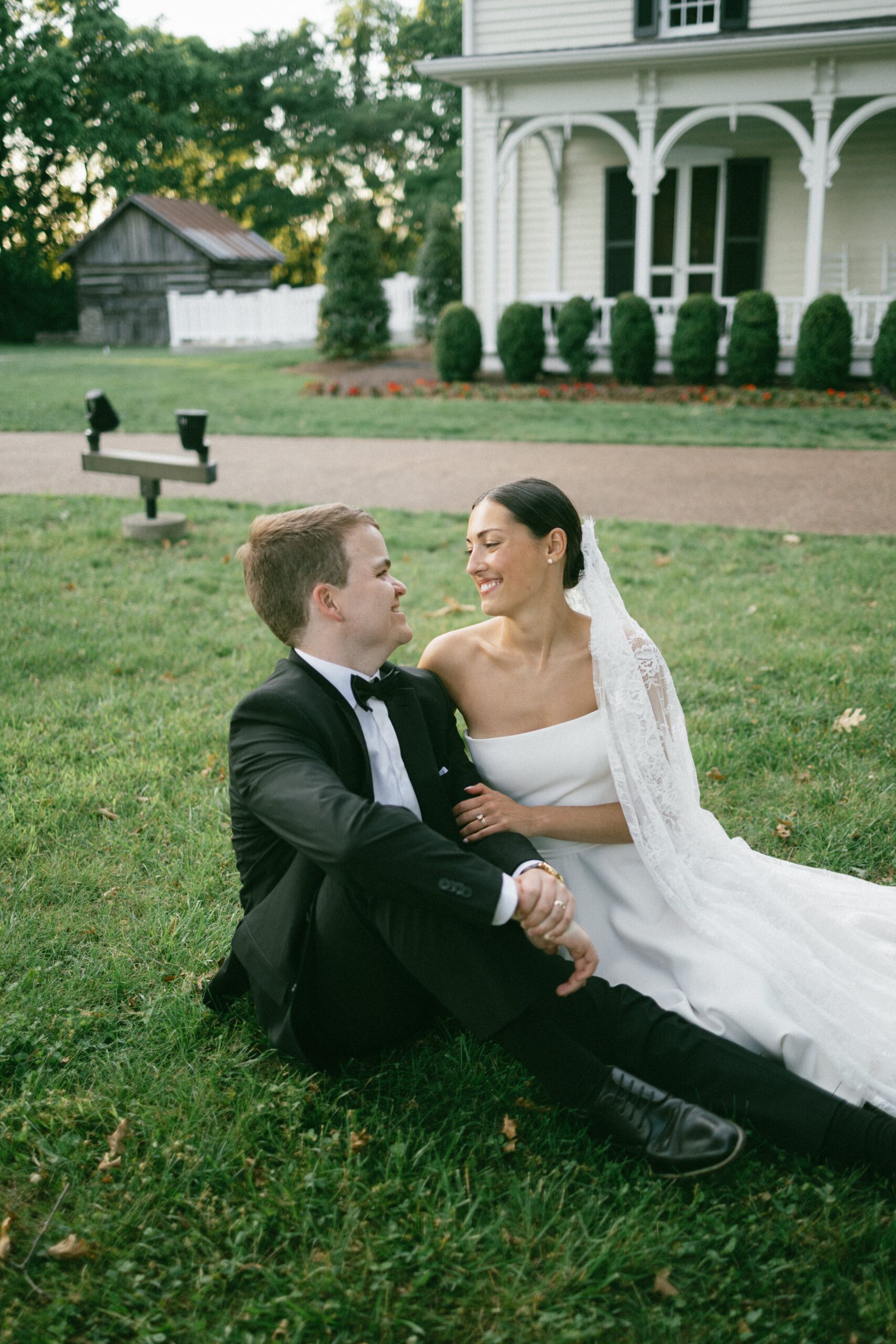 Newlywed couple smiling at each other while sitting on the lawn in front of a historic home at one of the charming small wedding venues in Nashville TN.