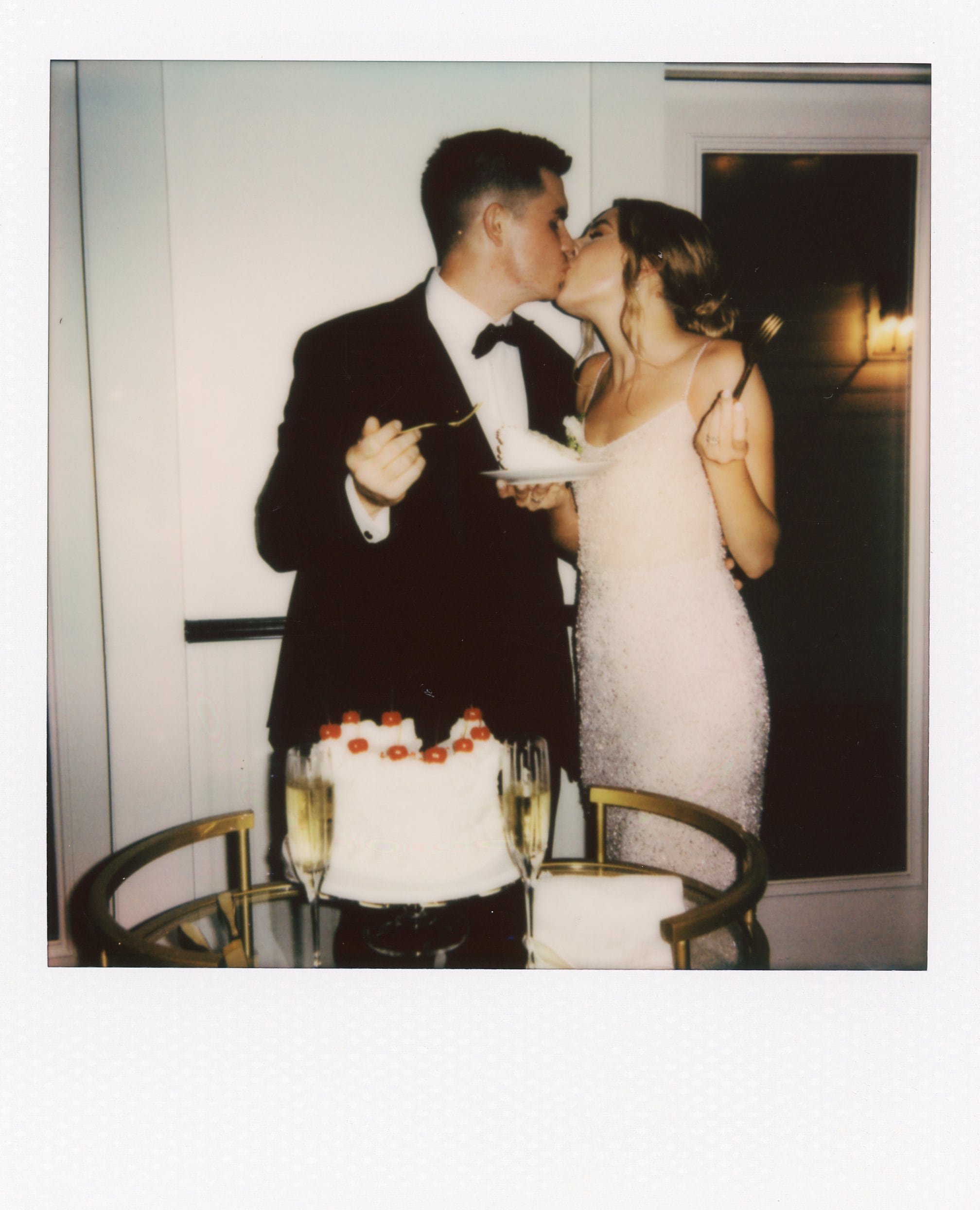 Bride and groom share a kiss while holding forks and standing beside their wedding cake at one of the charming small wedding chapels in Nashville TN.