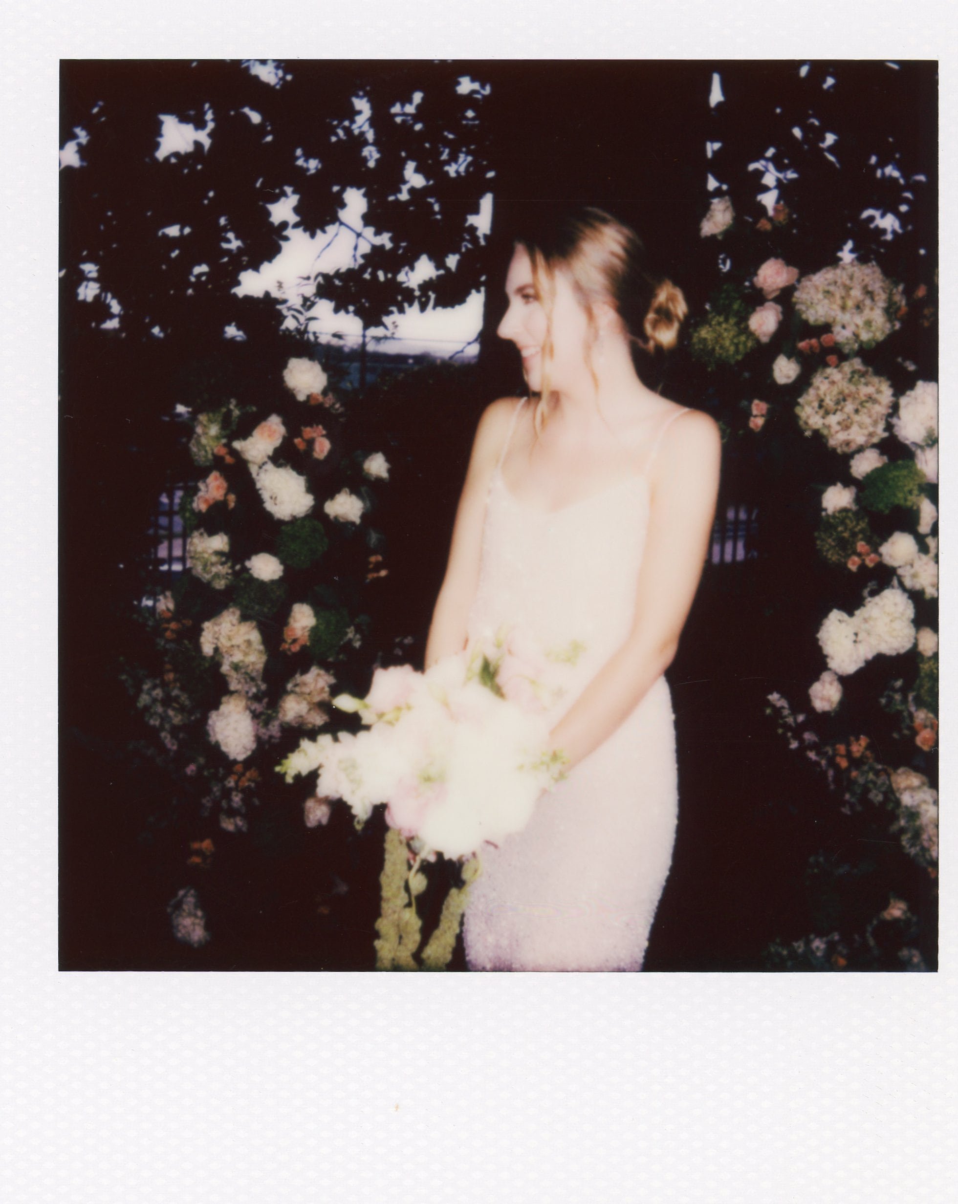 Bride holding a bouquet and smiling beneath a romantic floral arch during an evening celebration at one of the small wedding venues Nashville TN couples love.