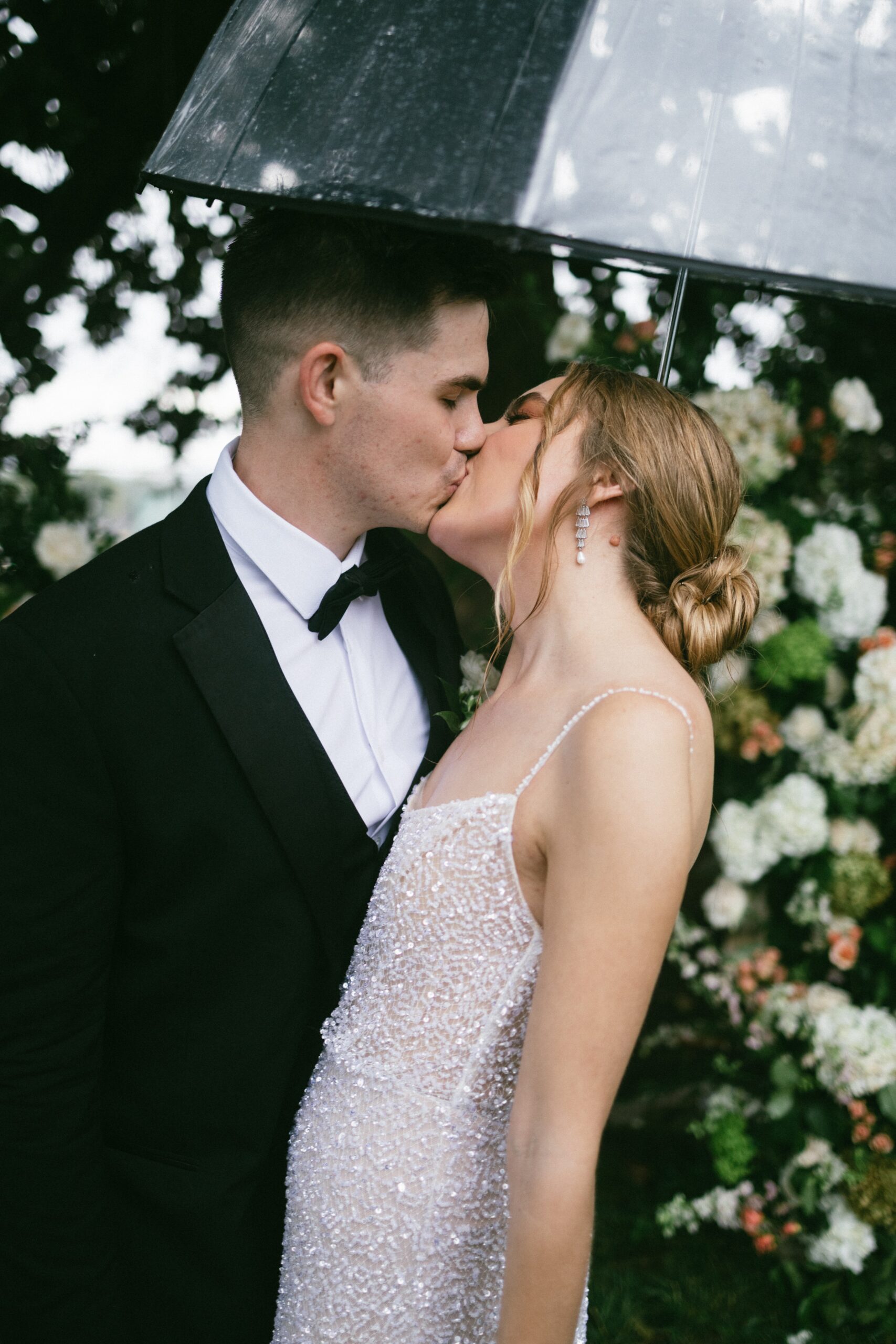Bride and groom sharing a kiss under a clear umbrella during a rainy wedding day at a small wedding venue in Nashville TN.