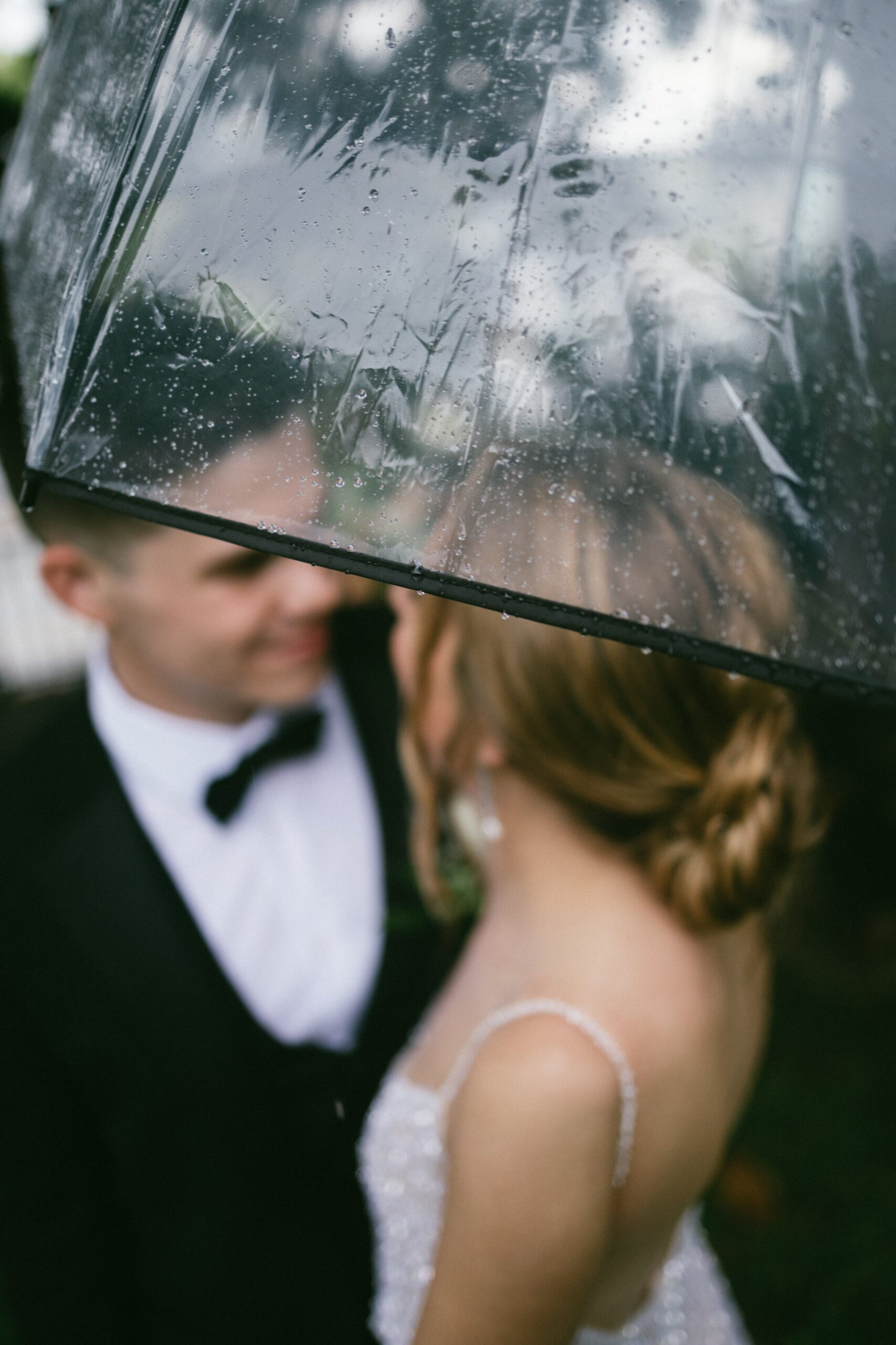 Bride and groom sharing a kiss under a clear umbrella during a rainy wedding day at a small wedding venue in Nashville TN.